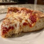 Close-up of a thick slice of cheese pizza with gooey, melted cheese stretching as it's lifted.