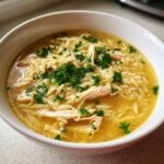 Close-up of a white bowl filled with amazing chicken orzo soup, featuring shredded chicken, orzo pasta, and fresh parsley.