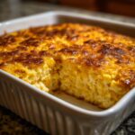 A close-up of a freshly baked, golden-brown corn pudding with a scoop removed, showing the creamy texture.
