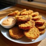 A plate piled high with crispy, golden fried green tomatoes served with a small bowl of spicy dipping sauce.