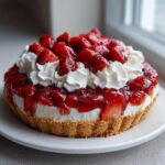 A close-up of a delicious strawberry pie with a graham cracker crust, creamy filling, strawberry glaze, and whipped cream dollops.