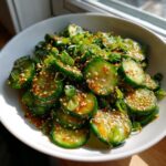 Close-up of vibrant asian cucumber salad slices tossed in dressing, topped with sesame seeds and green onions.