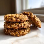 A stack of three chewy banana oatmeal cookies with one leaning against the side.