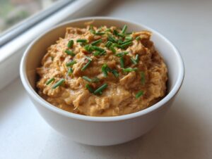 A close-up of homemade caramelized onion dip in a white bowl, garnished with fresh green chives.