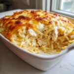 A close-up of creamy, baked chicken spaghetti casserole with a golden, bubbly cheese topping.