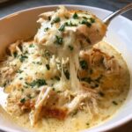 A spoonful of creamy chicken parmesan soup lifted from a bowl, showing melted, stretchy mozzarella cheese and shredded chicken.