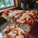 A hand holding up a thick slice of pizza showing the fluffy interior of the cottage cheese pizza crust with melted cheese.