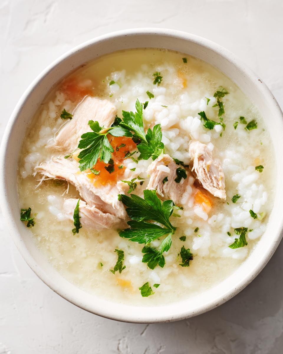 Overhead view of a white bowl filled with creamy chicken and rice soup, topped with shredded chicken and fresh parsley.
