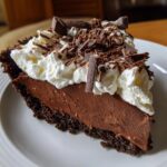 A decadent slice of chocolate cream pie featuring a thick chocolate filling, whipped cream, and chocolate shavings.