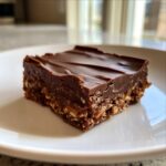 A single, rich square of homemade chocolate peanut butter fudge with a thick chocolate topping, sitting on a white plate.