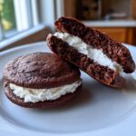 Two rich chocolate whoopie pies, one cut in half showing the thick white cream filling.
