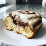 A close-up of a fluffy slice from the cinnamon roll cake recipe, topped with thick cream cheese frosting.