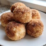 A close-up of five freshly baked cinnamon sugar snowball cookies piled on a white plate.