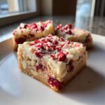 A close-up of a square cranberry bliss bars slice topped with white chocolate frosting and festive sprinkles.