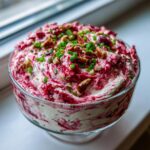 Close-up of vibrant cranberry jalapeno cream cheese dip swirled with red cranberry sauce, topped with pecans and chives.