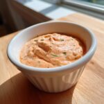 Close-up of creamy, orange-hued burger sauce speckled with herbs in a small white bowl.