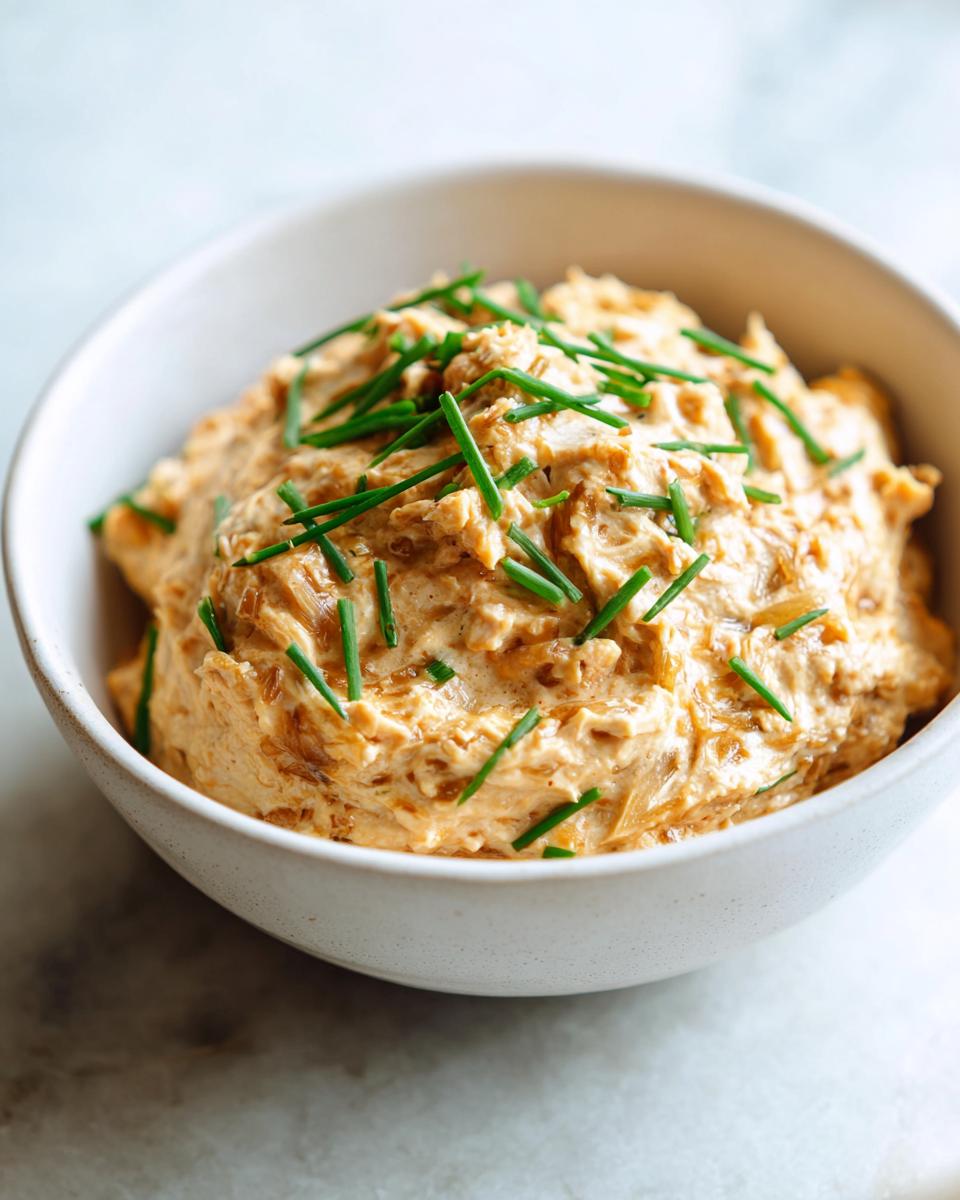 A close-up of rich, creamy caramelized onion dip topped generously with fresh green chives in a white bowl.
