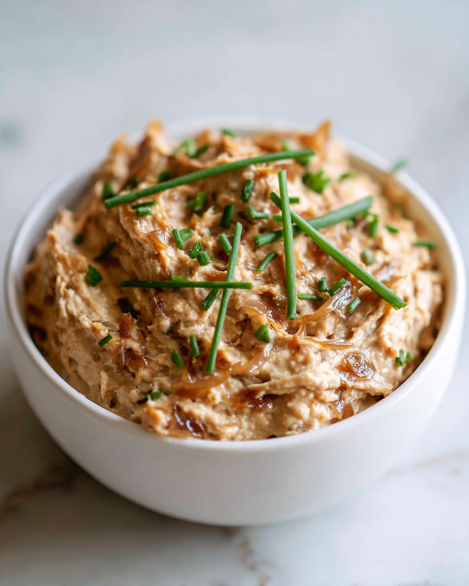 Close-up of creamy caramelized onion dip topped with fresh chives in a white serving bowl.