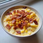 A close-up view of a bowl of creamy corn chowder loaded with corn kernels, potatoes, and crispy bacon bits.