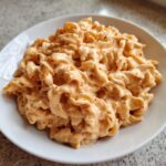 A close-up of creamy cottage cheese mac and cheese served in a white bowl, topped with red pepper flakes.