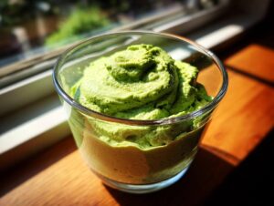 A vibrant green serving of creamy matcha chia pudding swirled high in a clear glass cup.