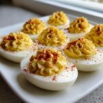 A plate of perfectly piped deviled eggs sprinkled with bright red paprika seasoning.