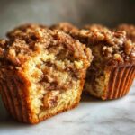 A close-up view of a pecan pie muffin cut in half, revealing a moist interior and crunchy pecan streusel topping.