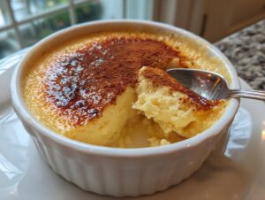 Close-up of a creamy egg custard in a white ramekin, showing a spoonful being taken out.