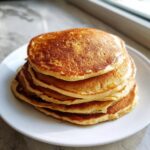 A tall stack of five golden brown, fluffy oatmeal pancakes served on a white plate.