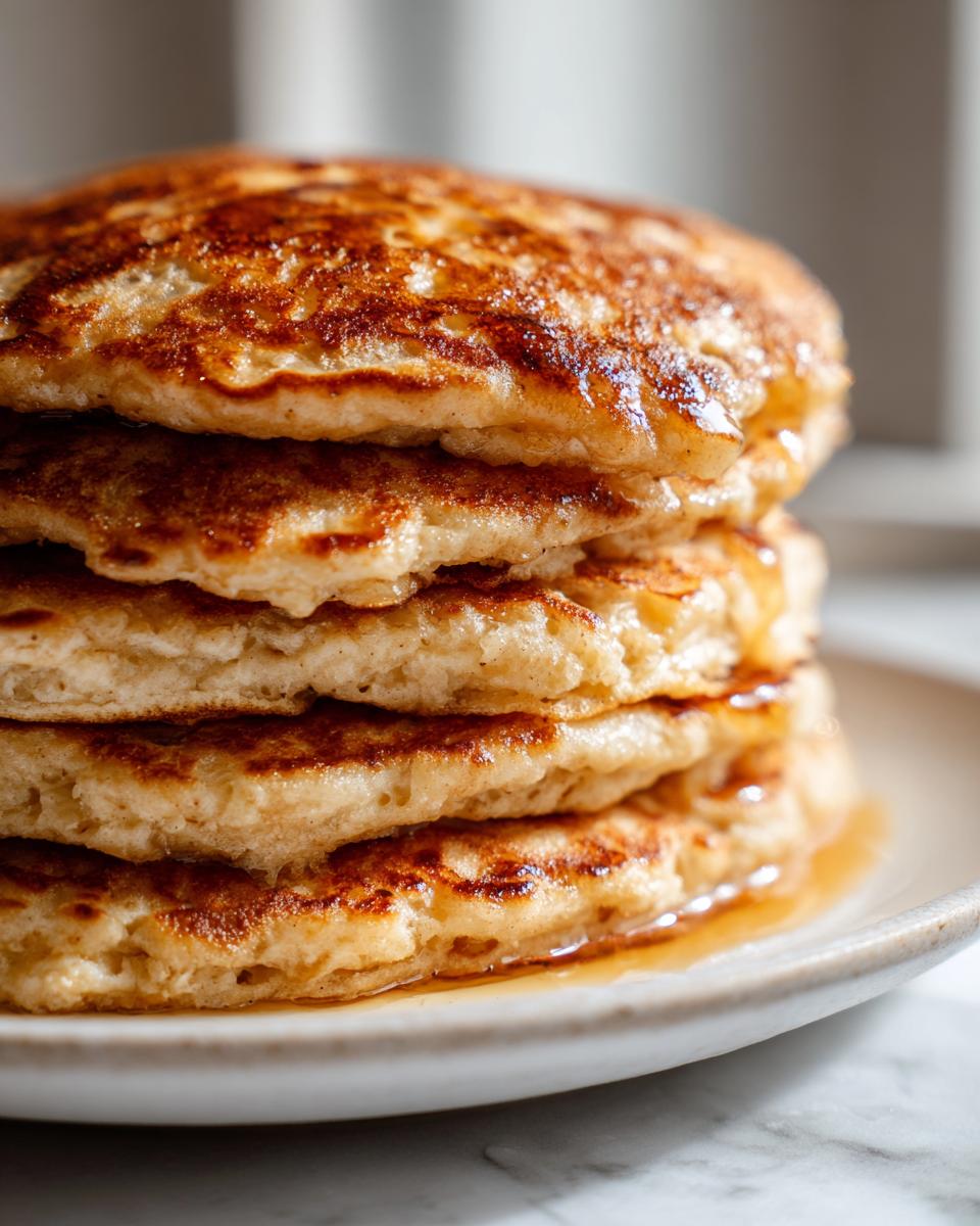 Close-up of a tall stack of fluffy oatmeal pancakes drizzled with golden syrup on a light plate.