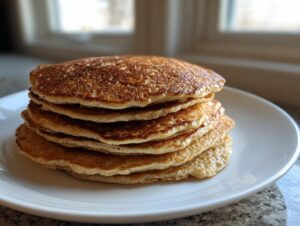 A tall stack of five golden brown oatmeal pancakes served on a white plate.