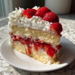 A perfect slice of strawberry shortcake cake showing layers of sponge, macerated strawberries, and whipped cream.