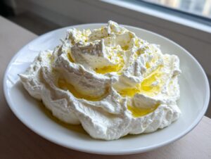 A close-up of creamy, fluffy whipped feta dip topped with golden olive oil and lemon zest.