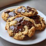 Close-up of several gooey, freshly baked chocolate chip cookies piled on a white plate.