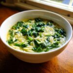 Close-up of a white bowl filled with vibrant italian orzo spinach soup, featuring orzo pasta and dark green spinach.