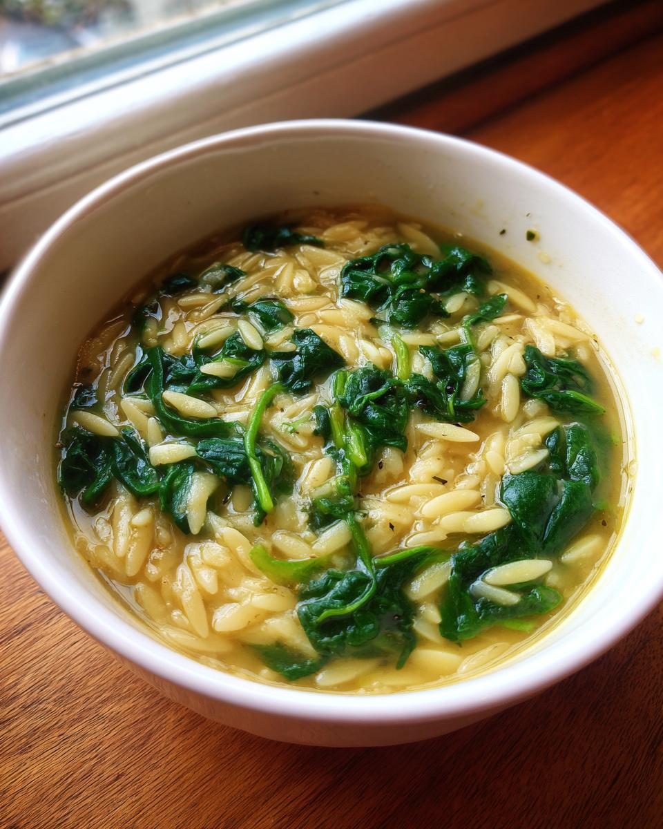 Close-up of a white bowl filled with Italian orzo spinach soup featuring yellow broth and bright green wilted spinach.