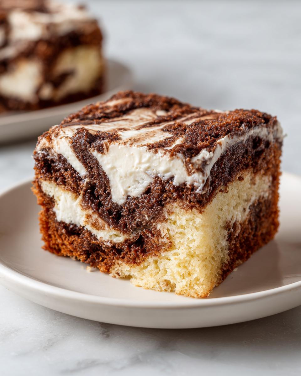 Close-up of a square slice of cinnamon roll cake featuring a marbled swirl of light cake, dark cinnamon filling, and cream cheese icing.