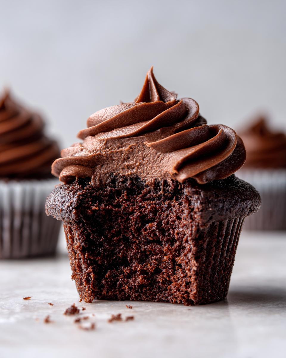 Close-up of a moist chocolate cupcake with a large swirl of rich chocolate frosting, showing the crumb texture.