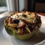 Close-up of a baked green bell pepper stuffed with shredded steak, onions, and melted cheese, resembling philly cheesesteak stuffed peppers.