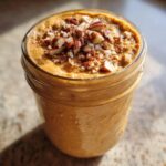 A close-up of creamy pumpkin pie overnight oats topped with chopped pecans in a glass jar.
