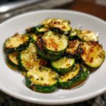 Close-up of golden brown, seasoned sauteed zucchini slices piled high in a white bowl.