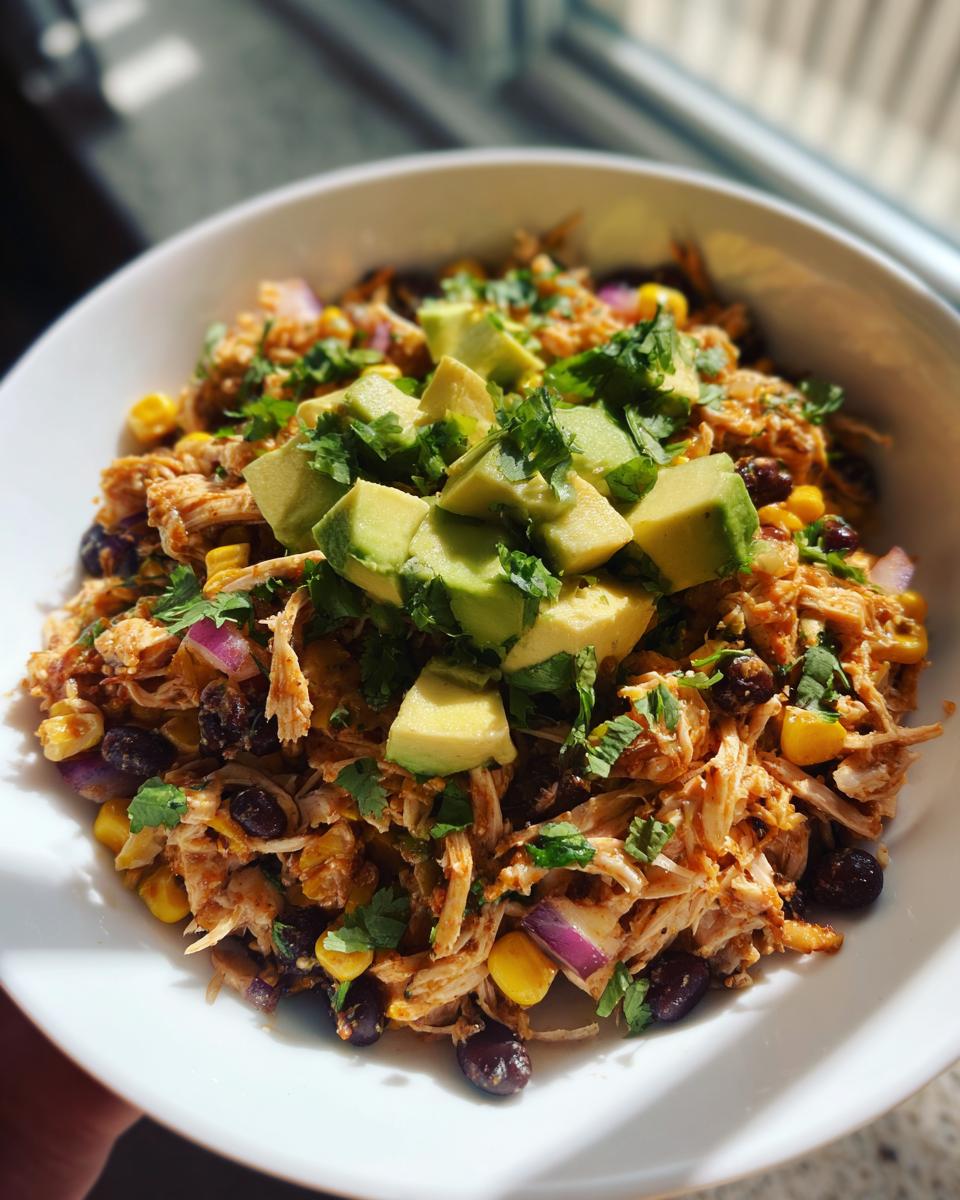 A vibrant bowl of shredded chicken high protein salad mixed with black beans, corn, red onion, and topped with diced avocado.