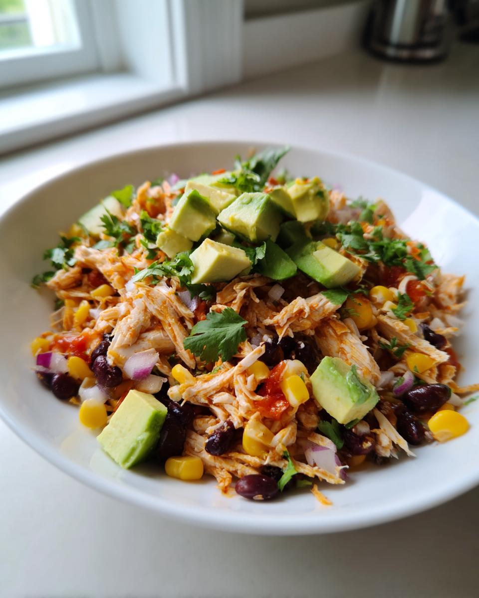 A vibrant bowl of shredded chicken high protein salad topped with diced avocado, black beans, corn, and cilantro.