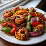 Close-up of flavorful, charred shrimp fajitas with colorful bell peppers and red onions on a white plate.