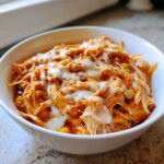 A close-up of shredded chicken chili topped with melted white cheese, likely slow cooker buffalo chicken chili.