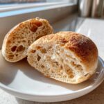 Close-up of a sourdough english muffin cut in half showing the airy, open crumb structure.