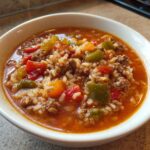 Close-up of a white bowl filled with steaming stuffed pepper soup, featuring ground meat, rice, and colorful bell pepper chunks.