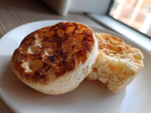 Two toasted sourdough english muffins showing their signature nooks and crannies on a white plate.