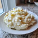 A generous serving of creamy, fluffy mashed potatoes piled high on a white plate.