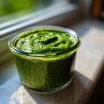Close-up of vibrant green matcha chia pudding texture in a small glass jar, sitting in sunlight.